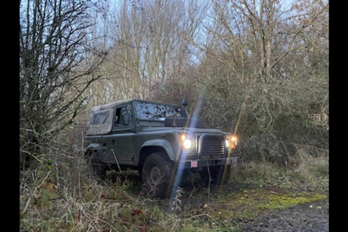 Off-road vehicle with headlights on in a wooded area.
