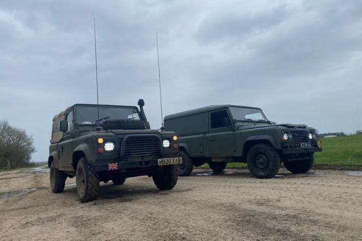Two military-style off-road vehicles on a dirt road under a cloudy sky.